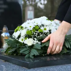 Dłoń kładzie wieniec na nagrobku. Pytanie, ile trwa żałoba w kościele katolickim, jest trudne.