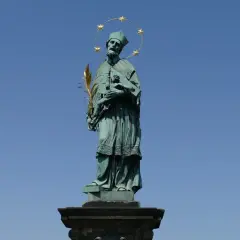 Pomnik św. Jana Nepomucena z gwiazdami nad głową i palmą męczeństwa w dłoni, na tle błękitnego nieba.