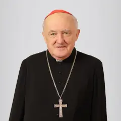 Uśmiechnięty biskup Nycz w czarnej sutannie i czerwonej zucchetto, z krzyżem na szyi.