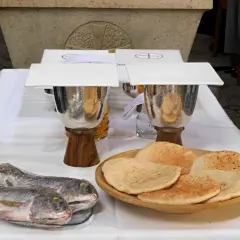 Dwa ryby i płaskie chleby na stole, symbolizujące rozmnożenie chleba i ryb.