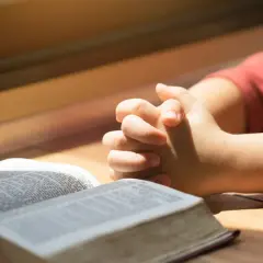 Dziecko z złożonymi dłońmi nad otwartą Biblią. To obraz modlitwy za córkę, pełen nadziei i wiary.