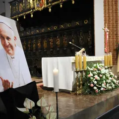 Papieski pontyfikat upamiętniony portretem i kwiatami w kościele.