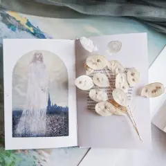Otwarta księga z ilustracją postaci w bieli i suszonymi lunariami. Obok tekst, który może zawierać najpiękniejsze rozważania drogi krzyżowej.