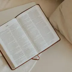 Otwarta Biblia, idealna do codziennej modlitwy. Na stronach widnieje tekst, a obok leży laptop.