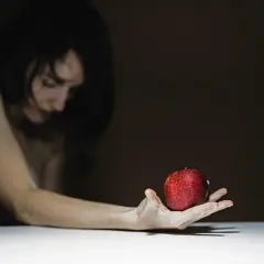 Kobieta z jabłkiem na dłoni, w ciemnym tle.