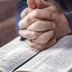 Dłonie złożone do modlitwy nad otwartą Biblią. Czas na nieszpory i refleksję.