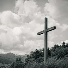 Drewniany krzyż na tle burzowych chmur, niczym biblijna góra, góruje nad zalesionym zboczem.
