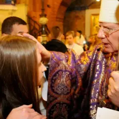 Biskup udziela sakramentu bierzmowania młodej dziewczynie, kładąc dłoń na jej głowie.