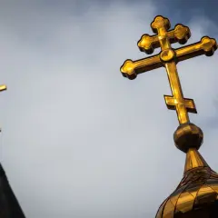 Złoty krzyż prawosławny lśni na tle pochmurnego nieba, symbolizując wiarę i nadzieję.