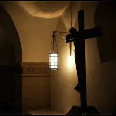 Ciemny krucyfiks i lampa oświetlają wnętrze kościoła. W ciszy rozbrzmiewa modlitwa "Ojcze nasz".
