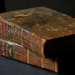 Dwa stare, skórzane tomy, jeden na drugim. Na grzbietach widoczne złote zdobienia i etykiety, jedna z nich zawiera fragment "psalm 15".