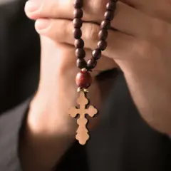 Dłonie trzymające drewniany różaniec z krzyżem, symbolizujące modlitwę do archanioła Rafała o uzdrowienie.