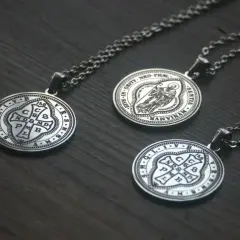 Trzy medaliki św. Benedykta na łańcuszkach, wykonane ze srebra, leżą na drewnianym tle.