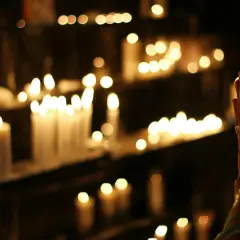 Dłonie złożone do modlitwy wieczornej do Matki Bożej, w blasku zapalonych świec.