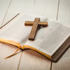 Otwarta Biblia z drewnianym krzyżem na stronach. Znajdź motywujące cytaty biblijne, które dodadzą Ci sił i nadziei.