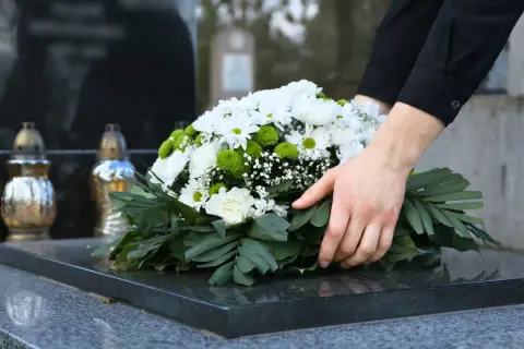 Dłoń kładzie wieniec na nagrobku. Pytanie, ile trwa żałoba w kościele katolickim, jest trudne.