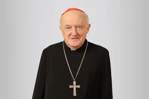Uśmiechnięty biskup Nycz w czarnej sutannie i czerwonej zucchetto, z krzyżem na szyi.