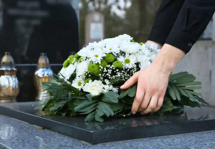 Dłoń kładzie wieniec na nagrobku. Pytanie, ile trwa żałoba w kościele katolickim, jest trudne.