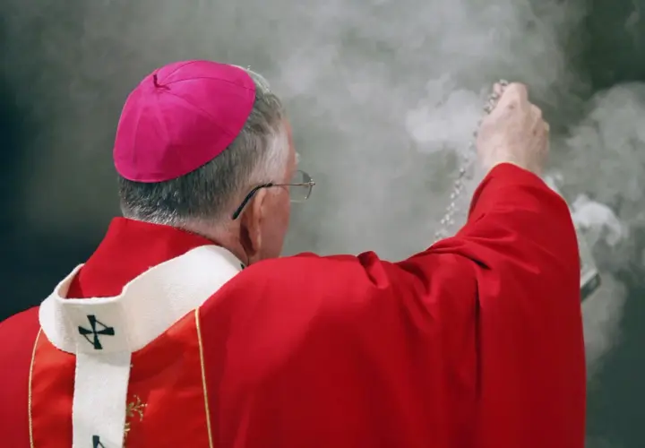 Biskup w czerwonej szacie i różowym birecie okadza powietrze. Czy to wpływa na to, ile zarabia ksiądz?