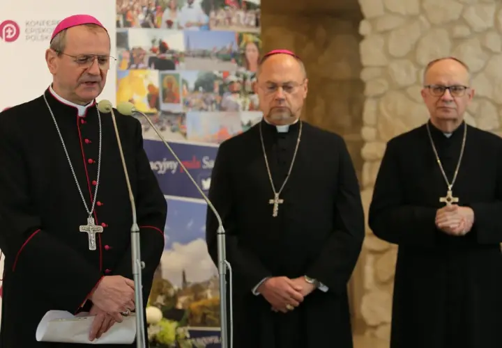 Trzech biskupów w czarnych szatach i z krzyżami na szyjach podczas zjazdu biskupów. Jeden z nich przemawia przy mikrofonie.