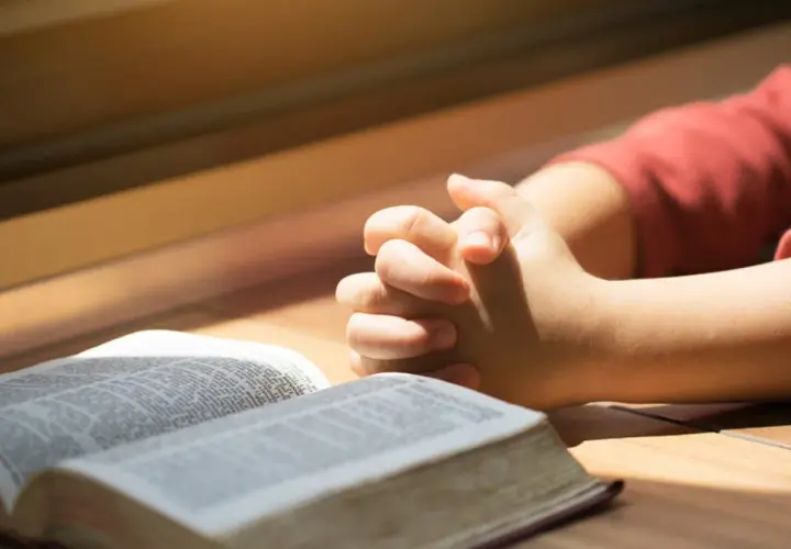 Dziecko z złożonymi dłońmi nad otwartą Biblią. To obraz modlitwy za córkę, pełen nadziei i wiary.