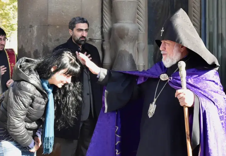 Błogosławieństwo kobiety przez duchownego w tradycyjnym ornamencie. Scena ukazuje głębokie korzenie armenia religia.