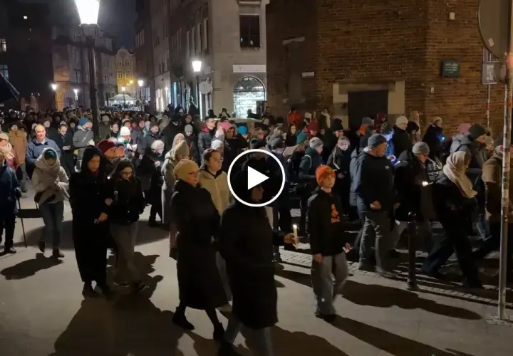 Tłum ludzi idzie ulicą nocą, trzymając świece. To wygląda jak Droga Krzyżowa.