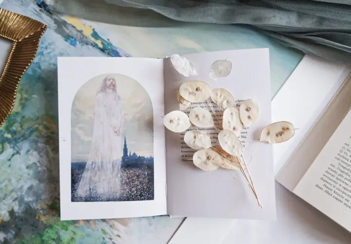 Otwarta księga z ilustracją postaci w bieli i suszonymi lunariami. Obok tekst, który może zawierać najpiękniejsze rozważania drogi krzyżowej.