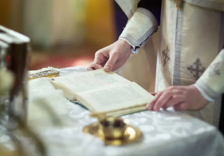 Dłoń duchownego trzyma księgę, czytając tekst. To może być fragment o tym, czym jest rezurekcja.