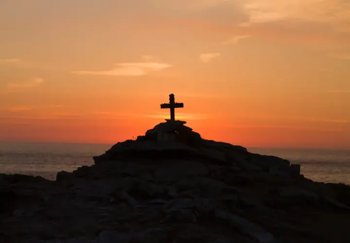 Kamienny krzyż na skalistym wzgórzu o zachodzie słońca, symbolizujący moment, kiedy umarł Jezus.