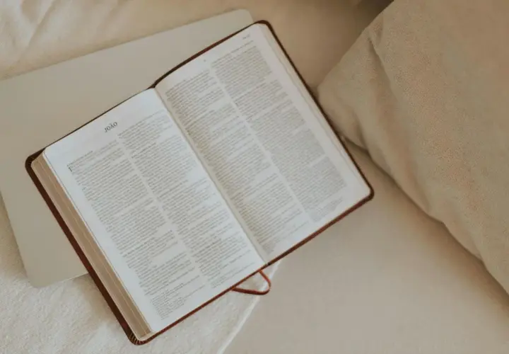 Otwarta Biblia, idealna do codziennej modlitwy. Na stronach widnieje tekst, a obok leży laptop.