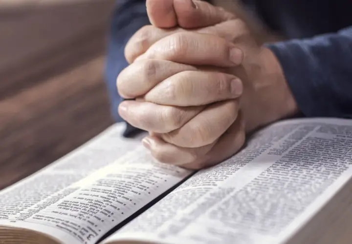 Dłonie złożone do modlitwy nad otwartą Biblią. Czas na nieszpory i refleksję.