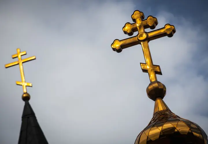 Złoty krzyż prawosławny lśni na tle pochmurnego nieba, symbolizując wiarę i nadzieję.
