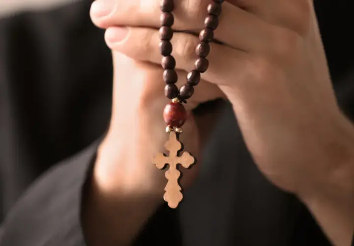 Dłonie trzymające drewniany różaniec z krzyżem, symbolizujące modlitwę do archanioła Rafała o uzdrowienie.