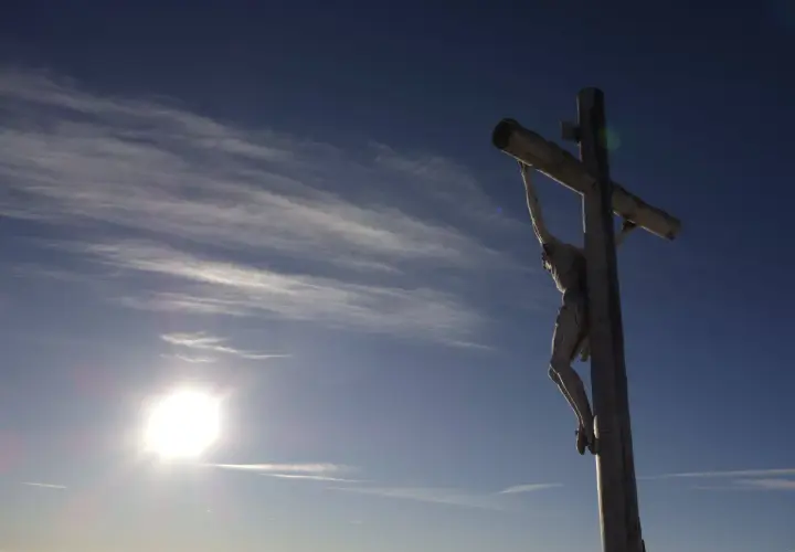 Drewniany krzyż z Jezusem na tle błękitnego nieba z chmurami. Słońce świeci jasno. Pamięć o tym, ile lat miał Jezus jak zmarł, jest wieczna.
