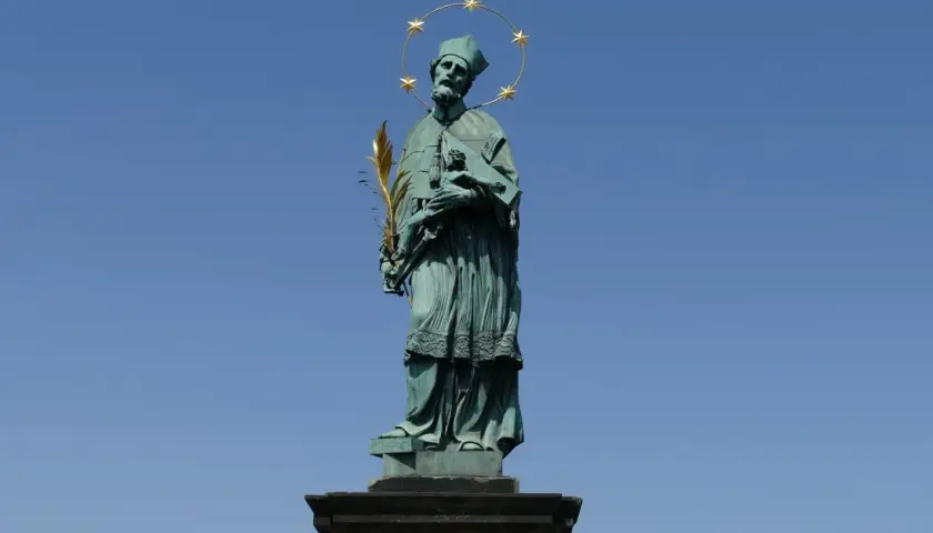 Pomnik św. Jana Nepomucena z gwiazdami nad głową i palmą męczeństwa w dłoni, na tle błękitnego nieba.