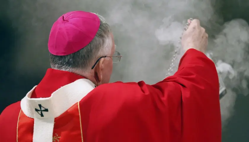 Biskup w czerwonej szacie i różowym birecie okadza powietrze. Czy to wpływa na to, ile zarabia ksiądz?