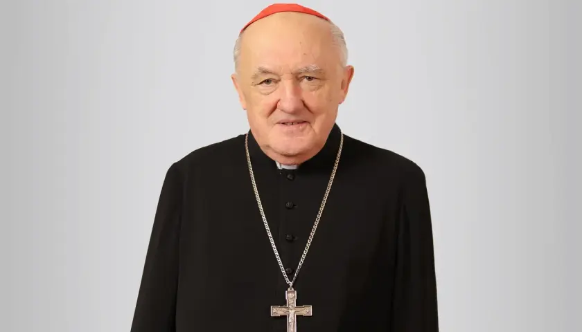 Uśmiechnięty biskup Nycz w czarnej sutannie i czerwonej zucchetto, z krzyżem na szyi.