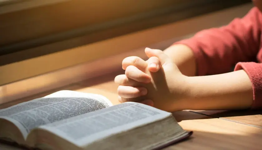 Dziecko z złożonymi dłońmi nad otwartą Biblią. To obraz modlitwy za córkę, pełen nadziei i wiary.