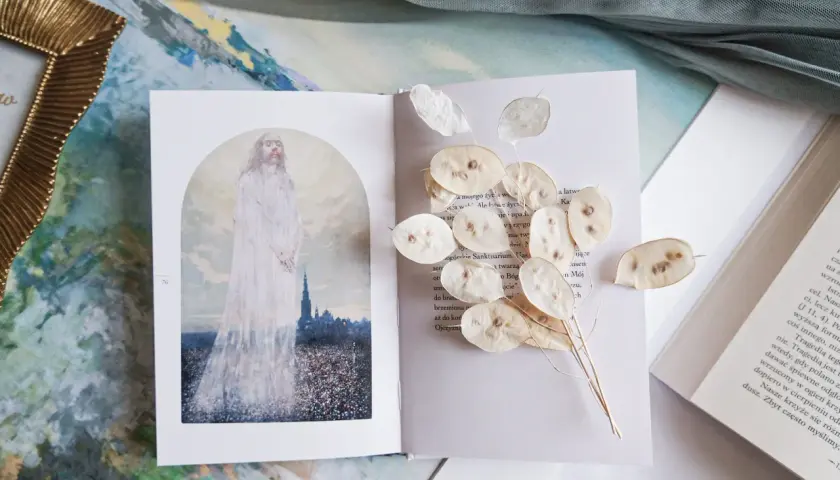 Otwarta księga z ilustracją postaci w bieli i suszonymi lunariami. Obok tekst, który może zawierać najpiękniejsze rozważania drogi krzyżowej.