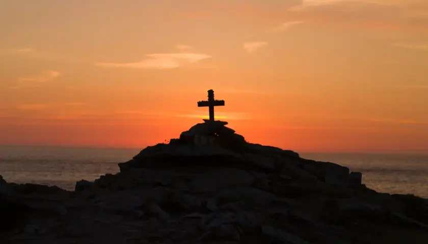 Kamienny krzyż na skalistym wzgórzu o zachodzie słońca, symbolizujący moment, kiedy umarł Jezus.