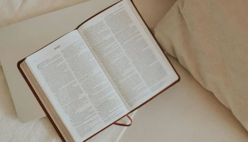 Otwarta Biblia, idealna do codziennej modlitwy. Na stronach widnieje tekst, a obok leży laptop.
