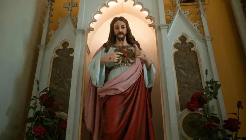 Figurka Jezusa z Sercem, wskazująca na nie, mówi "jestem który jestem". Czerwone róże u stóp.