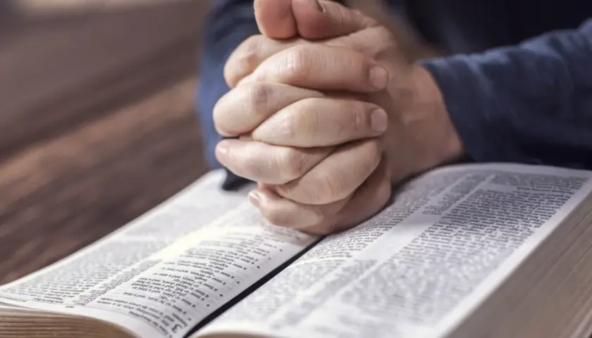 Dłonie złożone do modlitwy nad otwartą Biblią. Czas na nieszpory i refleksję.