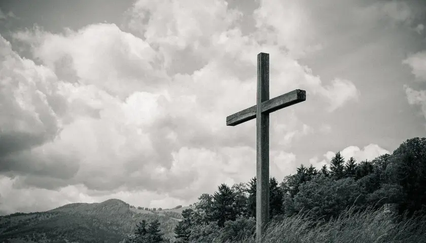 Drewniany krzyż na tle burzowych chmur, niczym biblijna góra, góruje nad zalesionym zboczem.
