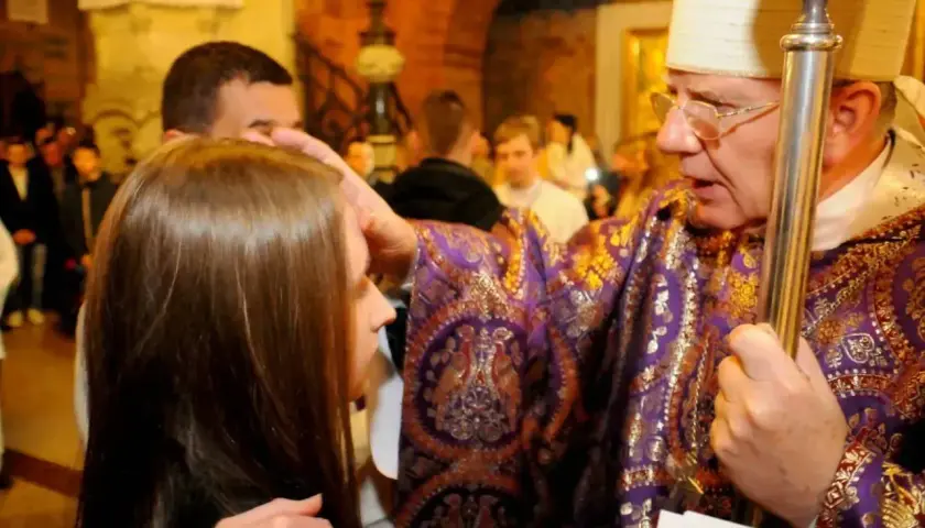 Biskup udziela sakramentu bierzmowania młodej dziewczynie, kładąc dłoń na jej głowie.