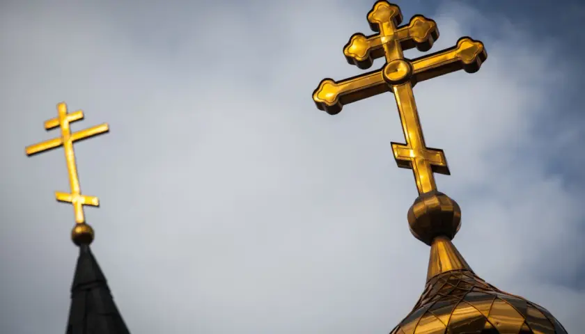 Złoty krzyż prawosławny lśni na tle pochmurnego nieba, symbolizując wiarę i nadzieję.