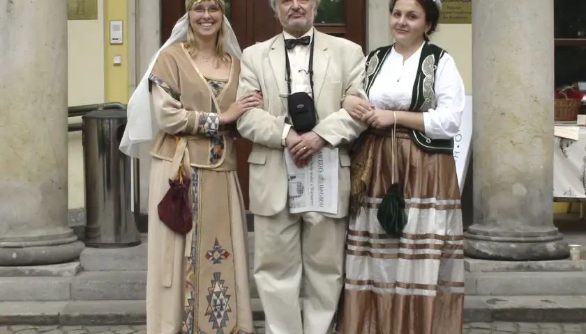 Ormianie w Polsce. Trzy osoby w strojach ludowych, dwie kobiety w tradycyjnych sukniach i mężczyzna w garniturze, pozują przed muzeum.