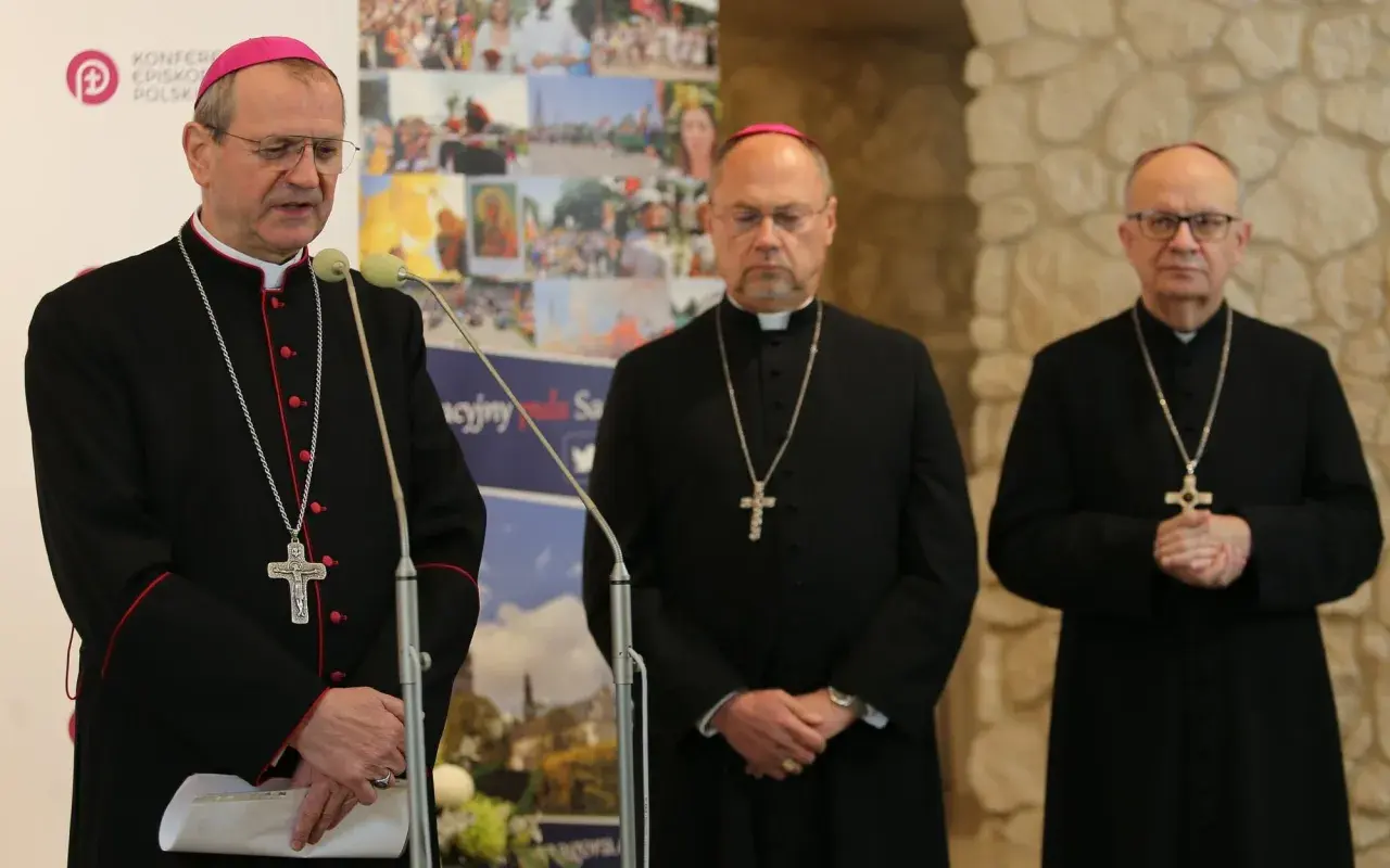 Trzech biskupów w czarnych szatach i z krzyżami na szyjach podczas zjazdu biskupów. Jeden z nich przemawia przy mikrofonie.