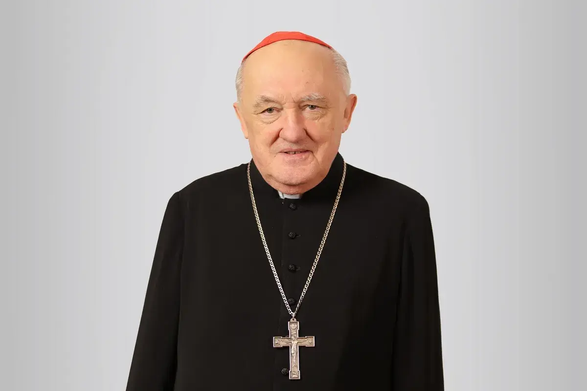 Uśmiechnięty biskup Nycz w czarnej sutannie i czerwonej zucchetto, z krzyżem na szyi.